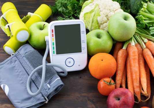 Blood pressure monitor,dumbbells and fresh fruits with vegetables against wooden table. Healthy lifestyle and prevention of hypertension concept